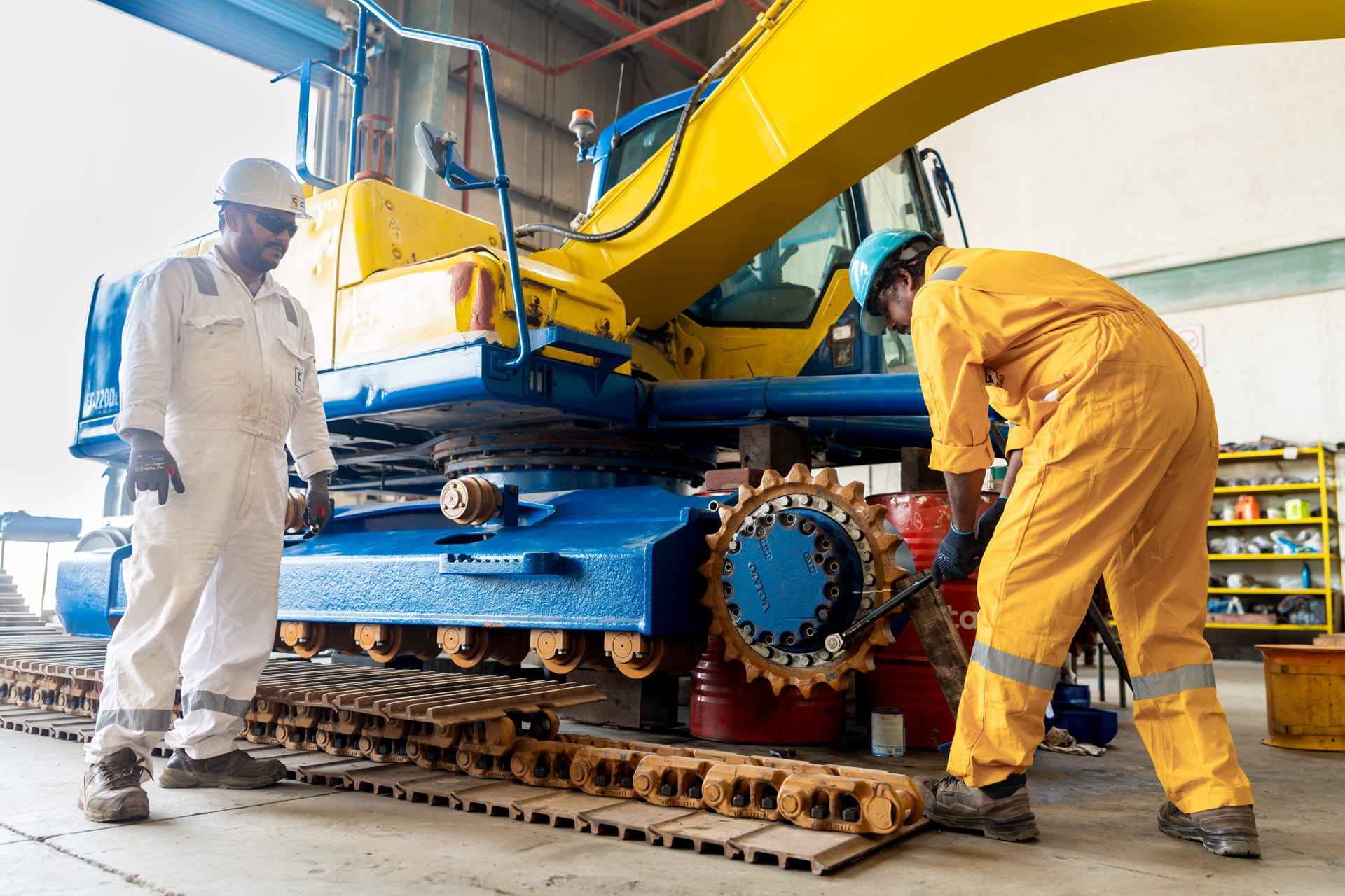Yellow and blue tracked excavator raised on blocks in a workshop with its track removed.