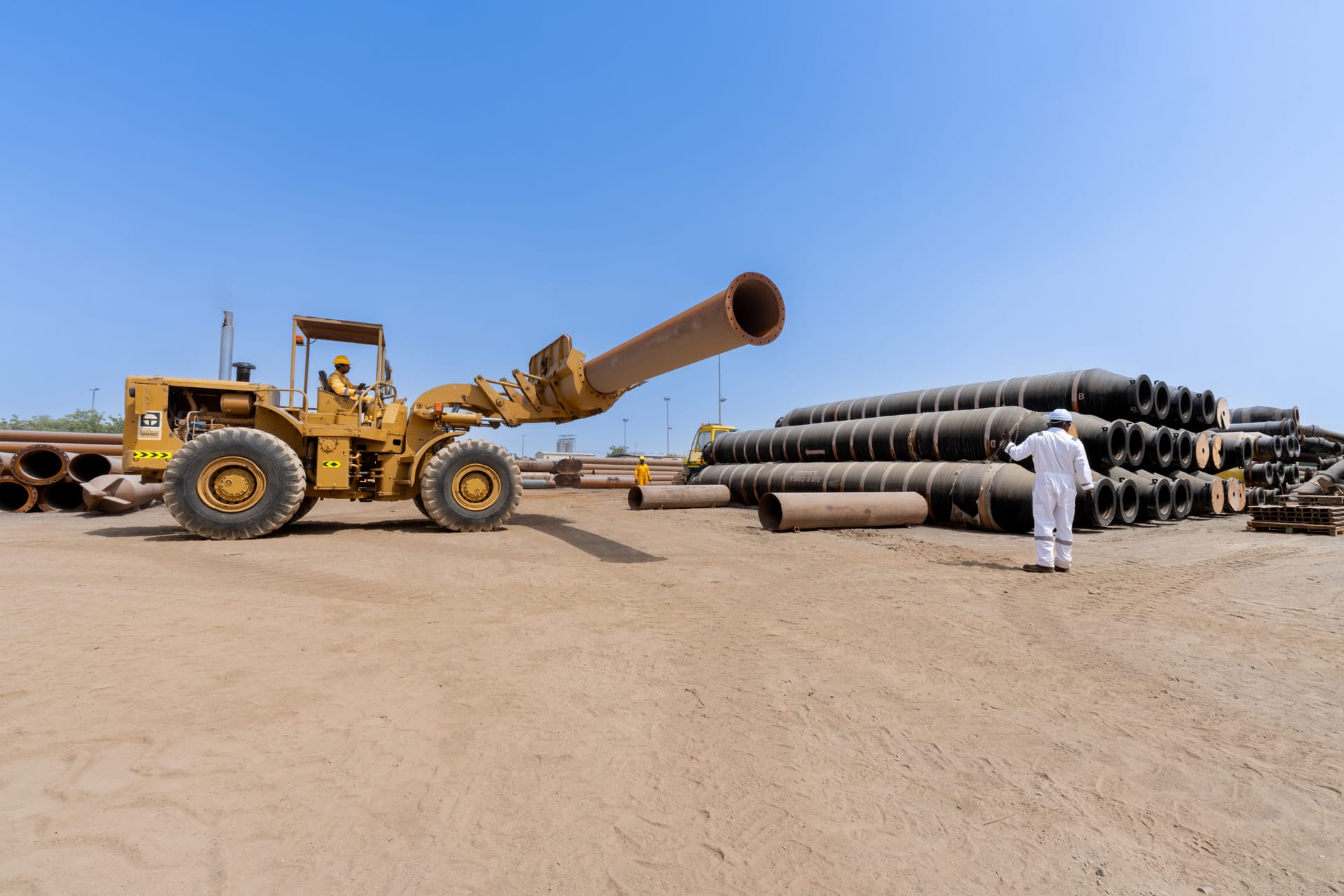 Yellow 966C wheel loader raising a long dredging pipe with a worker inspecting floating pipes.