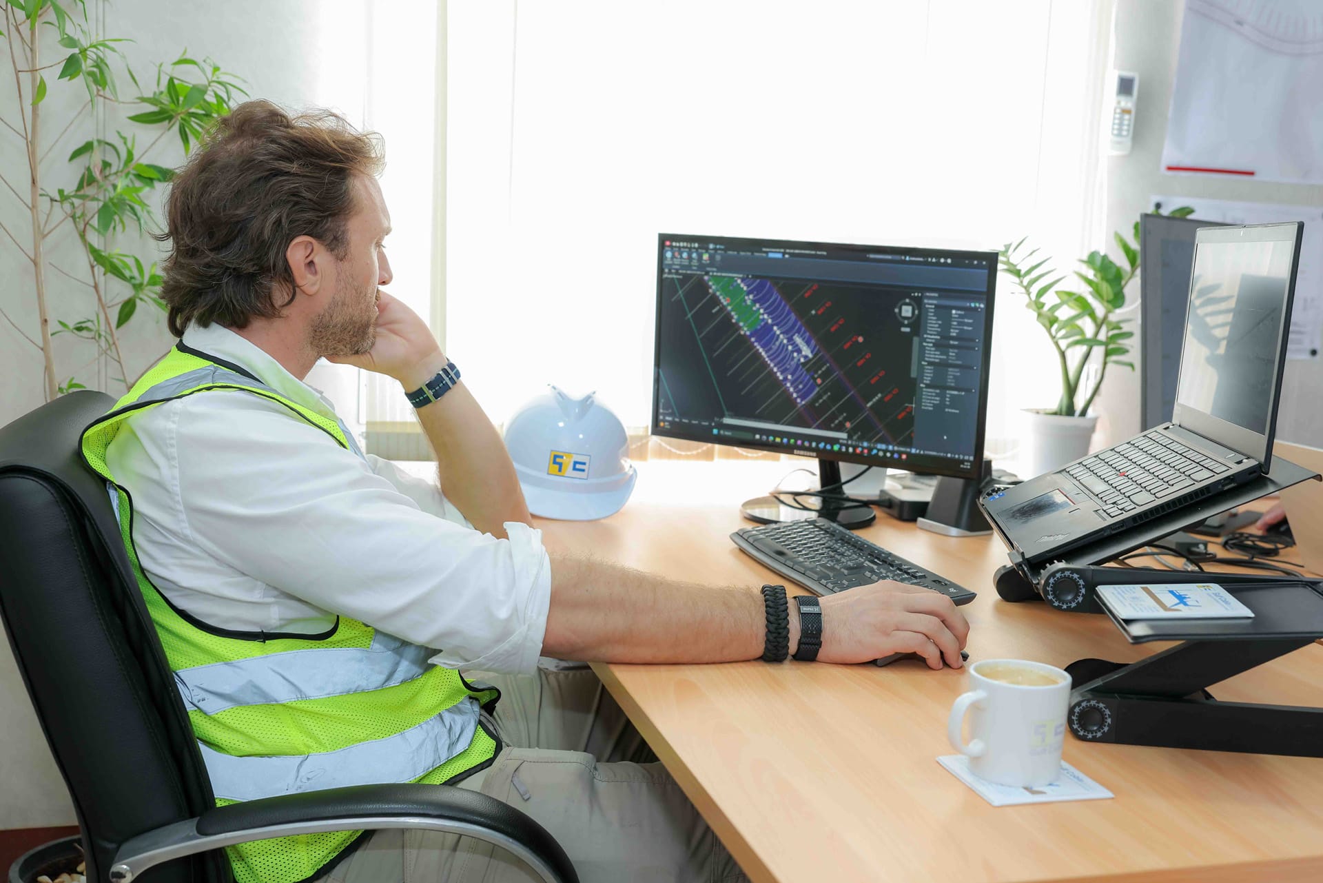 Engineer in a high-visibility vest working on a CAD dredging plan beside a Gulf Cobla branded hard hat.