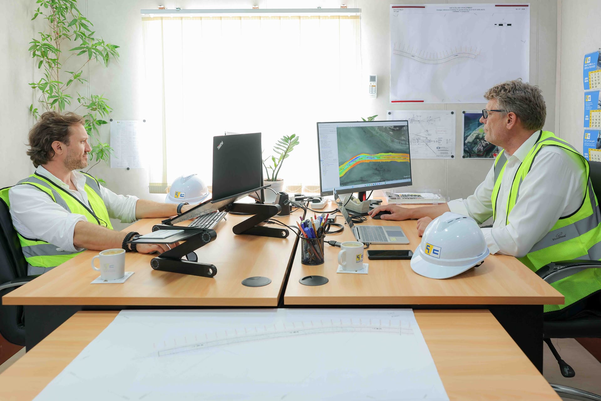 Two engineers discussing a coloured channel survey on screen in a Gulf Cobla project office.