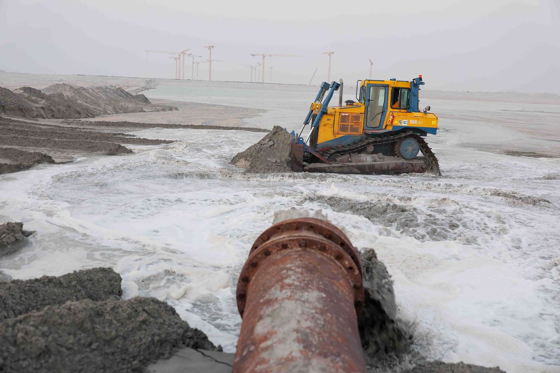 Gulf Cobla D6R XW tracked dozer pushing sand beside a slurry discharge outfall on a reclamation site.