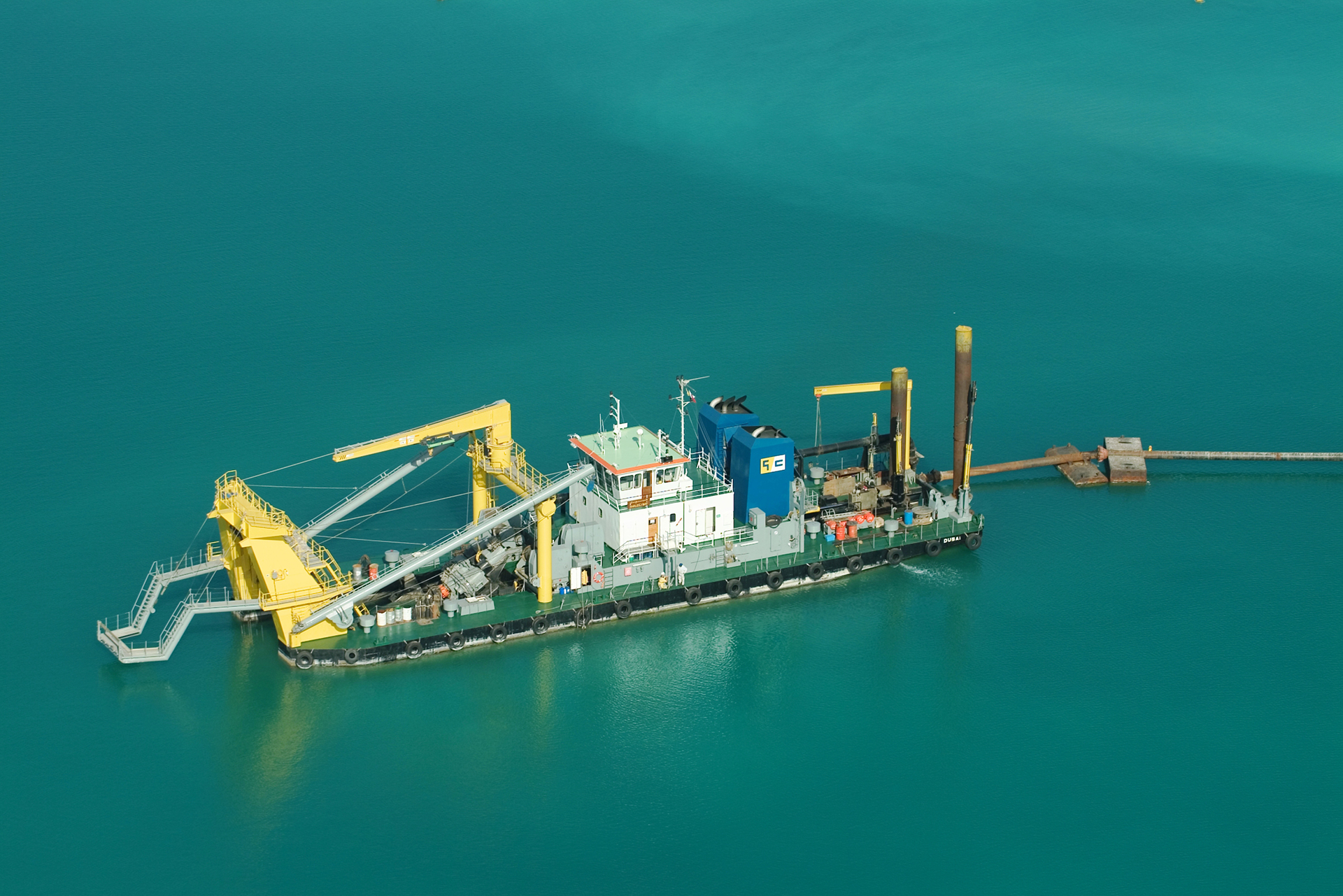Close view down a dredger ladder to the toothed cutter head and suction pipe at the waterline.