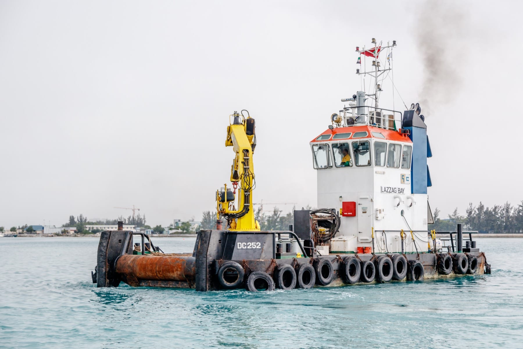 The multicat Lazzag Bay, registered DC 252, under way with its yellow deck crane stowed and tyre fenders along the hull.