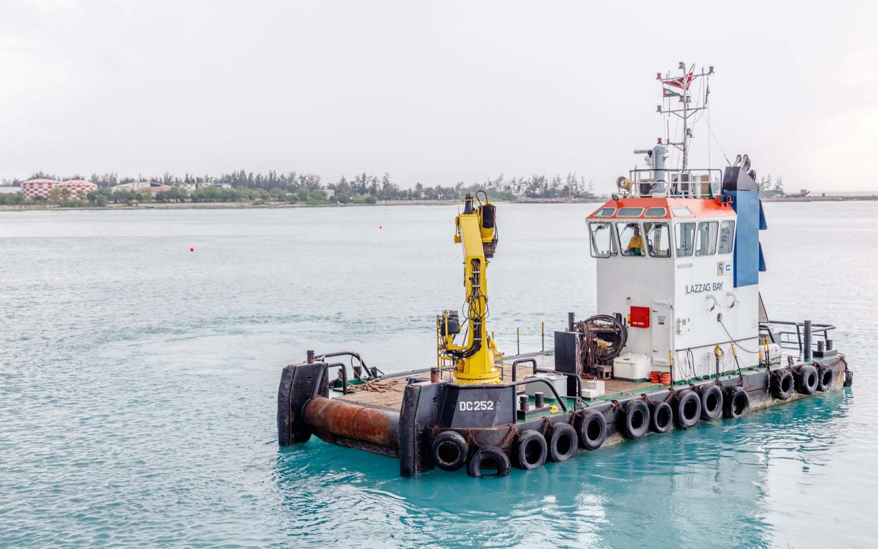 The multicat Lazzag Bay sitting on calm water, deck crane and towing gear visible.