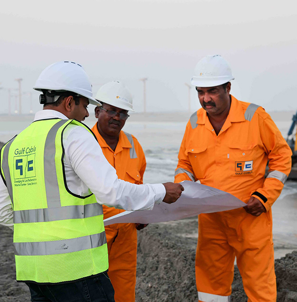 Engineers gathered around a table reviewing a set of marine works drawings.